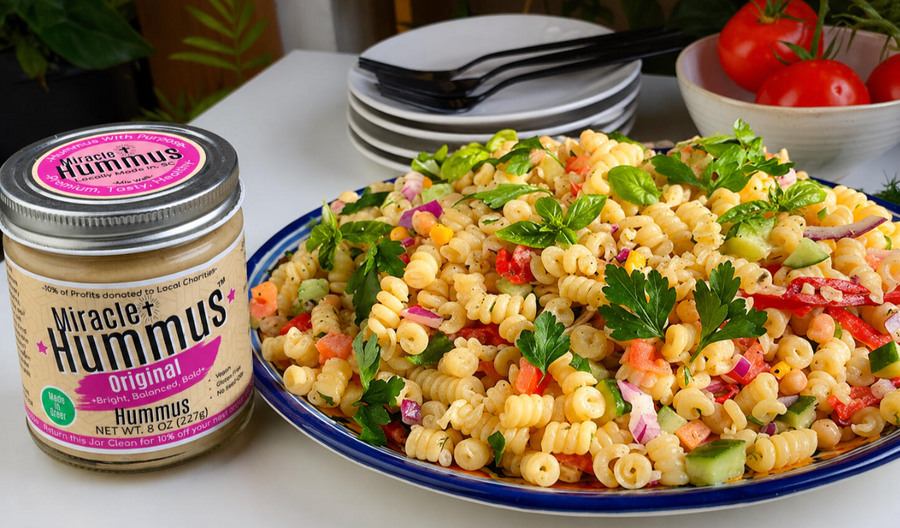 Pasta salad with vegetables on a plate next to a jar of Good Hummus.